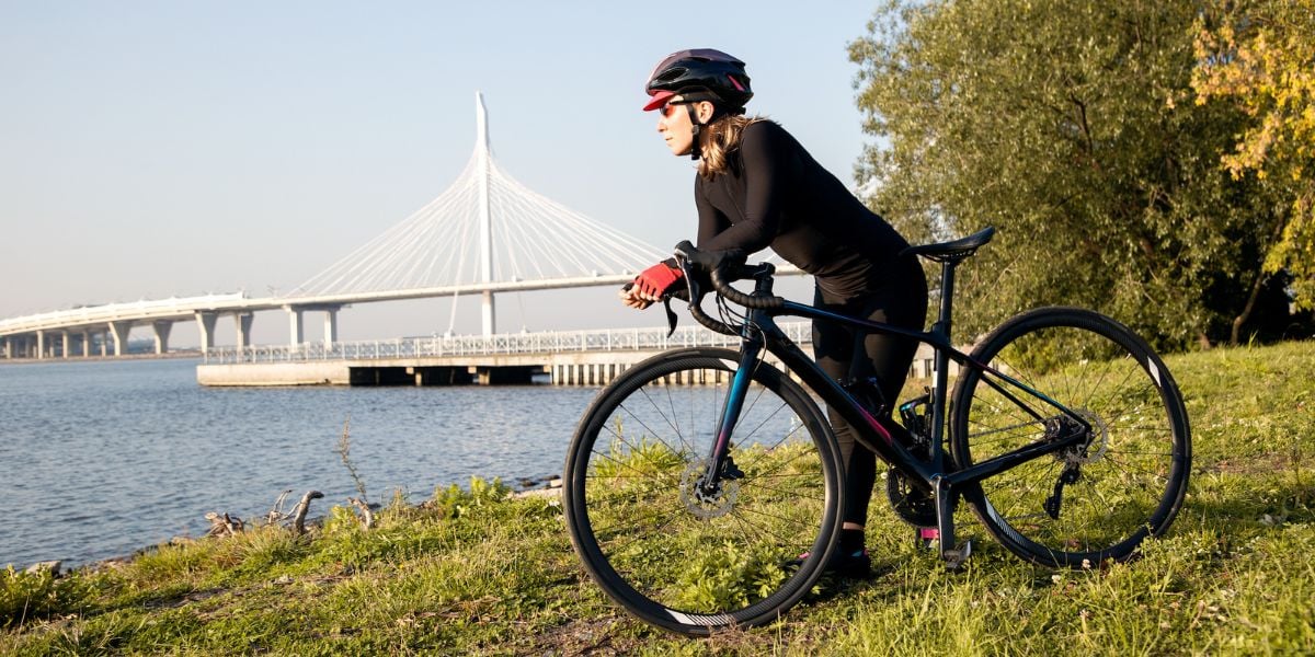 Mustapukuinen pyöräilijä ja polkupyörä meren rannalla, taustalla silta.